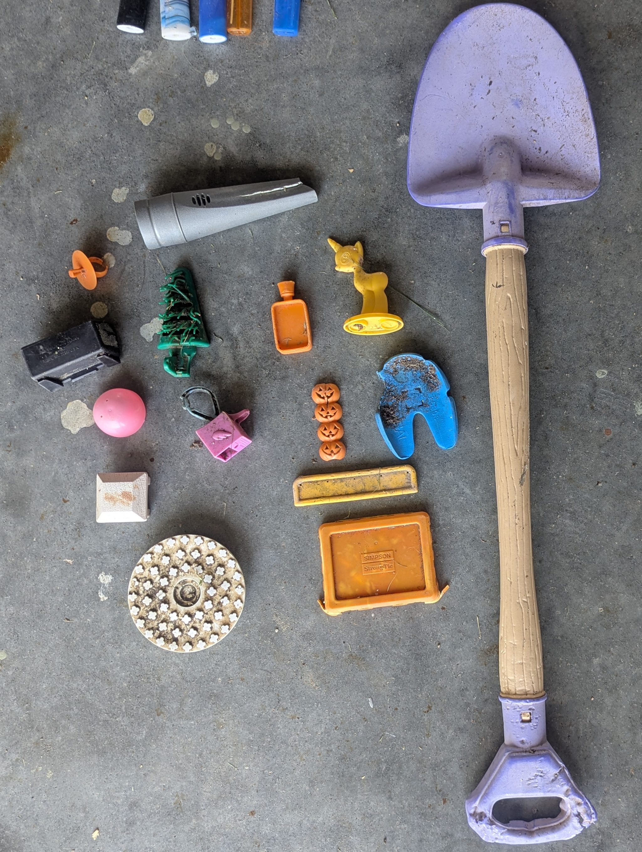 A collection of found items including a purple plastic shovel, various small toys and objects, and debris arranged on a flat surface.